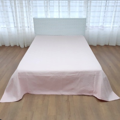 Cama com cabeceira branca e colcha rosa clara num quarto com cortinas brancas