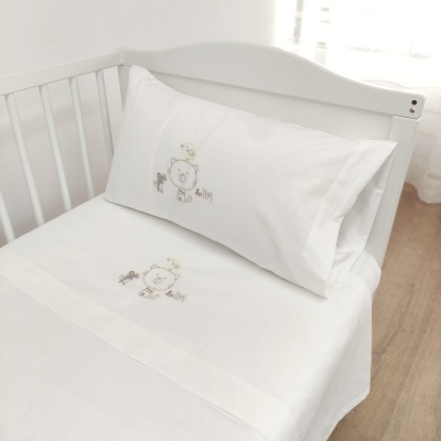 Lençóis de berço brancos com ursinho e bordado 'hello!' num berço branco