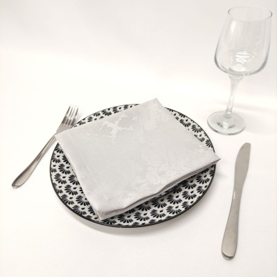 Conjunto de talheres, prato com padrão preto e branco, guardanapo branco e copo de vinho transparente