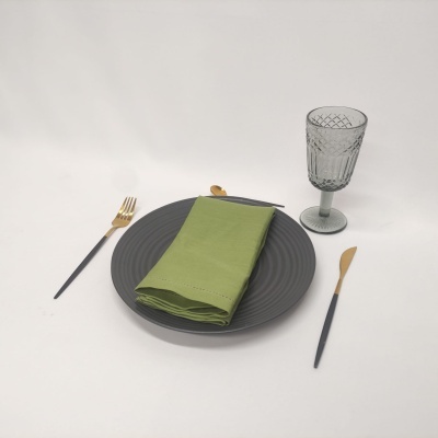 Conjunto de mesa com prato cinzento, guardanapo verde, talheres dourados e copo de vidro cinzento