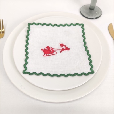 Guardanapo branco com borda verde e desenho de trenó vermelho numa mesa posta