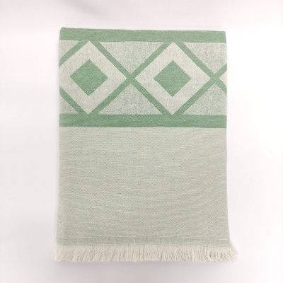 Toalha dobrada com padrão geométrico verde e bege e franjas na extremidade