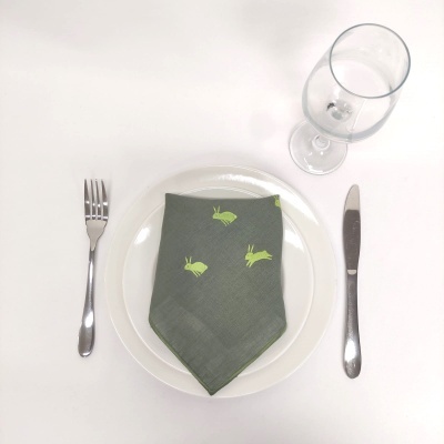 Mesa posta com prato branco, guardanapo verde com insetos amarelos, talheres de metal e copo de vidro