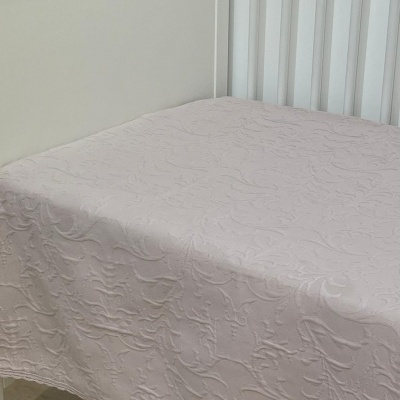 Colcha rosa claro texturizada numa cama branca com cabeceira em ripas