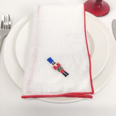 Guardanapo branco com bordas vermelhas e um soldadinho de chumbo bordado sobre pratos brancos
