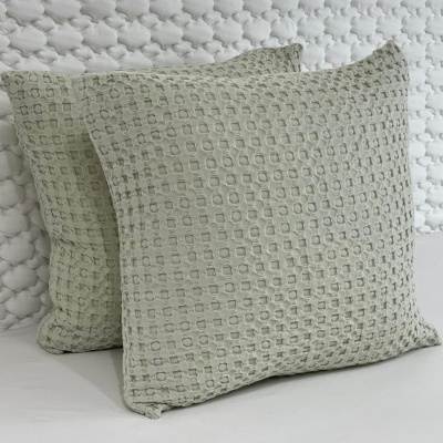 Duas almofadas cinza claro com padrão texturizado de quadrados sobre fundo branco com padrão de nuvens