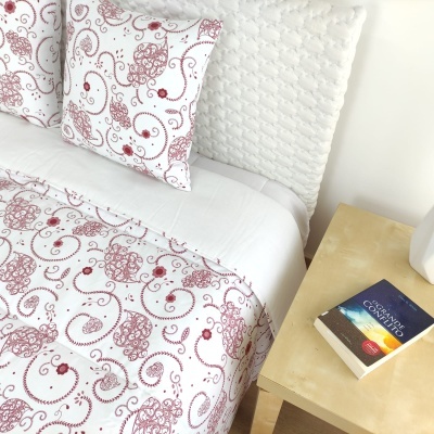 Conjunto de cama vermelho e branco com padrão floral e livro sobre mesa de madeira clara