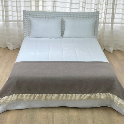 Cama com cabeceira acolchoada, roupa de cama branca e coberta cinza com borda cremosa