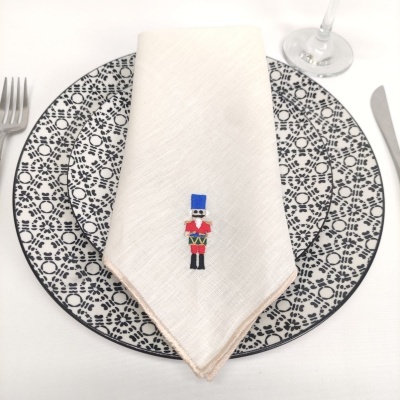 Guardanapo branco com borda bege e soldado bordado em prato com padrão preto e branco