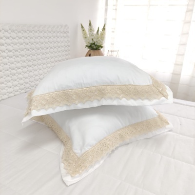 Almofadas brancas com borda em renda bege sobre cama branca