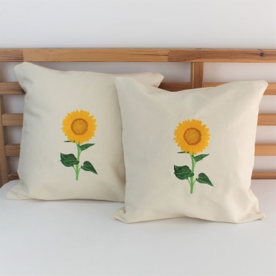 Duas almofadas brancas com bordado de girassol em suporte de madeira.