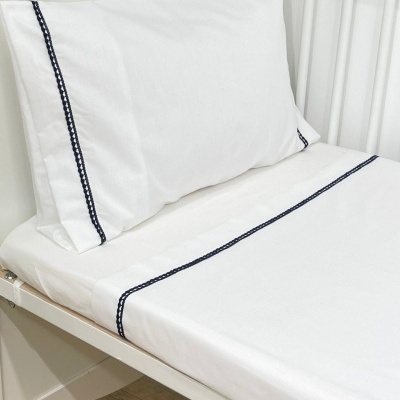 Cama infantil branca com lençóis brancos decorados com linhas azul-escuras