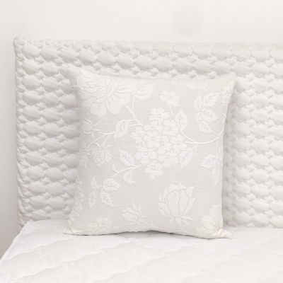 Almofada branca com padrão floral sobre cama branca acolchoada