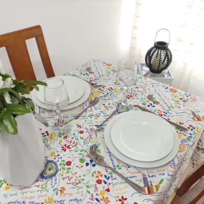 Mesa de jantar posta com toalha colorida, pratos brancos, talheres, copos, vaso com planta e lanterna preta