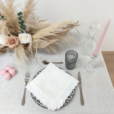 Mesa posta com prato decorado, guardanapo branco, talheres, copo cinza, vela rosa em castiçal e arranjo floral seco