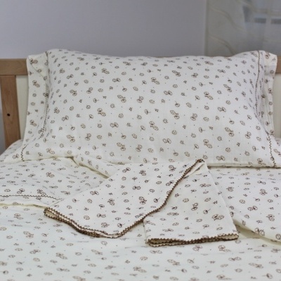 Conjunto de roupa de cama creme com padrão floral castanho numa cama de madeira clara