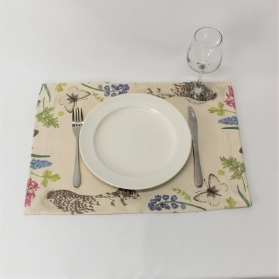 Mesa posta com prato branco, talheres metálicos, copo de vidro e individual de tecido estampado.