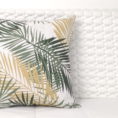 Almofada decorativa branca com folhas verdes e amarelas sobre colchão branco