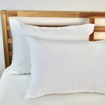 Duas almofadas brancas texturizadas numa cama com cabeceira de madeira