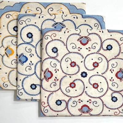 Guardanapos quadrados de pano com bordado floral e arabescos coloridos em fundo creme