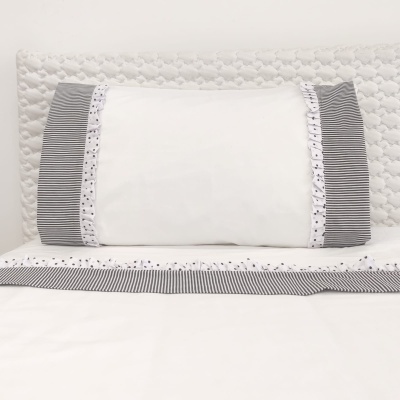 Fronha branca com laterais às riscas pretas e brancas sobre cama com lençol branco