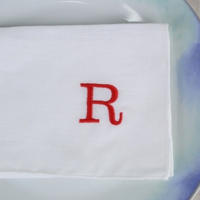 Guardanapo branco com letra R vermelha sobre prato azul e branca com talheres ao lado