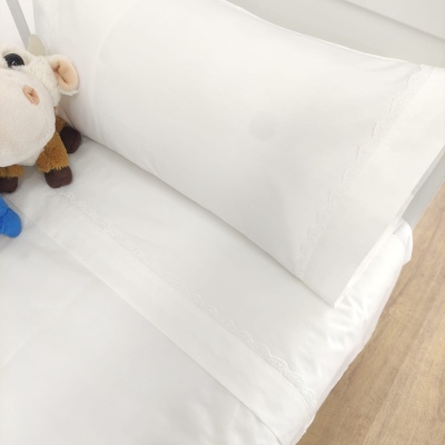 Roupa de cama branca com renda e brinquedo de vaca de peluche num ambiente de quarto