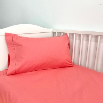 Lençol e almofada cor de coral em berço branco