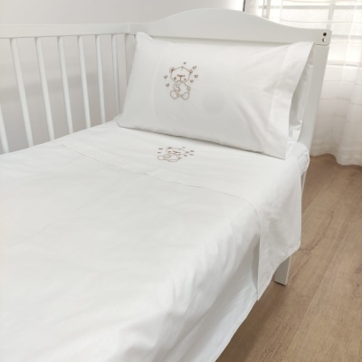 Cama de criança branca com lençóis brancos e urso bordado