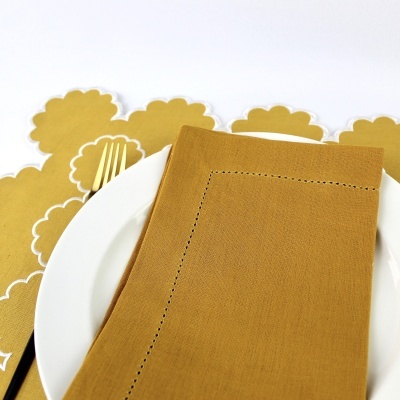 Guardanapo amarelo mostarda sobre prato branco com garfo dourado e bases para pratos amarelas onduladas