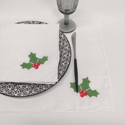 Jogo americano e guardanapo brancos com folhas verdes e bagas vermelhas sobre mesa