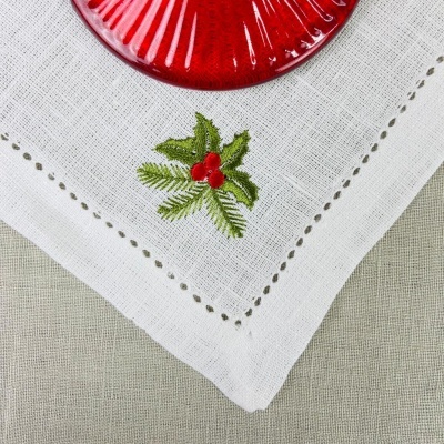 Guardanapo branco bordado com folhas e bagas vermelhas ao lado de prato vermelho