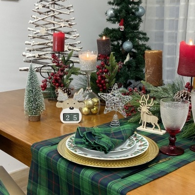 Mesa de Natal com toalha xadrez, pratos decorados, velas e enfeites natalícios.
