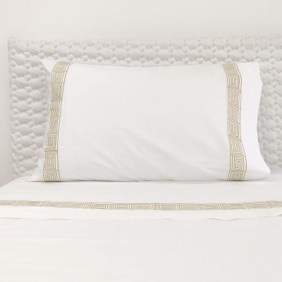 Almofada branca com bordado bege decorativo sobre cama com colchão branco texturizado