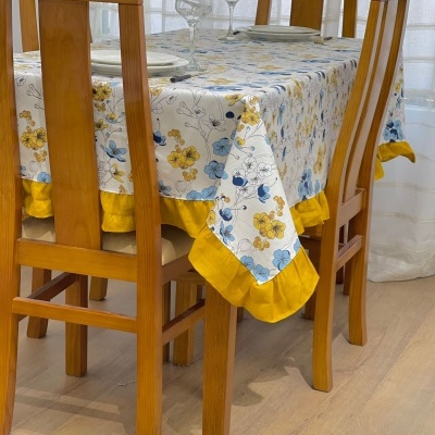 Mesa de madeira com toalha de flores e bainha amarela, quatro cadeiras, copos e pratos
