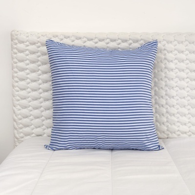 Almofada azul às riscas numa cama com cabeceira branca acolchoada