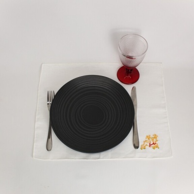 Prato preto, talheres, copo de vinho vermelho e guardanapo branco bordado sobre mesa branca