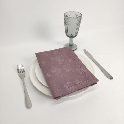 Conjunto de louça branca com talheres de metal, guardanapo rosa com flores e copo de vidro verde
