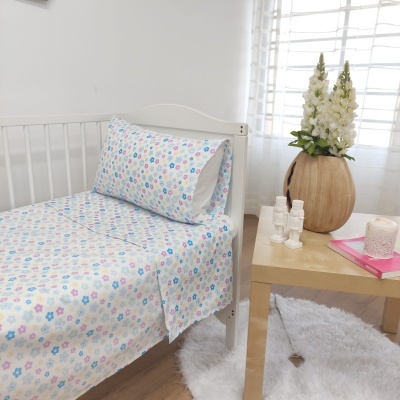 Lençóis de berço com padrão de flores coloridas numa cama branca ao lado de uma mesa decorativa