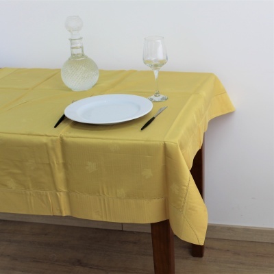 Toalha de mesa amarela com prato branco, talheres pretos, copo e garrafa de vidro numa mesa de madeira