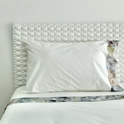 Almofada branca com cabeceira de tecido branco trançado e faixa floral pastel na cama