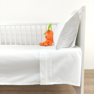 Berço branco com roupa de cama branca, almofada e peluche laranja