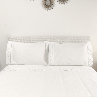 Conjunto de almofadas brancas com fronhas de pontos pequenos e cabeceira cinzenta com espelhos decorativos na parede