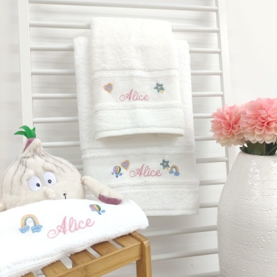 Toalhas de banho e rosto brancas com bordado e nome Alice junto a brinquedo de pelúcia e flores cor de rosa