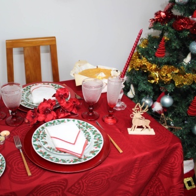 Mesa posta para Natal com decoração vermelha e verde junto a uma árvore de Natal decorada