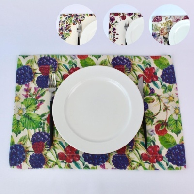 Prato branco com talheres sobre individual de tecido com padrão de frutas vermelhas e folhas verdes.