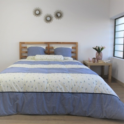 Cama arrumada com colcha azul e creme floral e cabeceira de madeira
