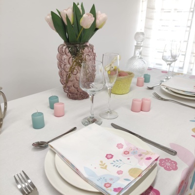 Mesa de jantar decorada com toalha floral, guardanapo, pratos, talheres, vasos, flores tulipas e velas coloridas