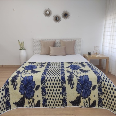 Quarto com cama decorada com manta floral azul e almofadas bege, mesa de cabeceira e decoração minimalista.