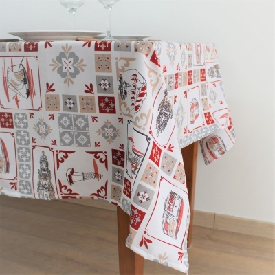 Toalha de mesa estampada com padrões geométricos e desenhos decorativos em tons vermelhos e bege numa mesa de madeira